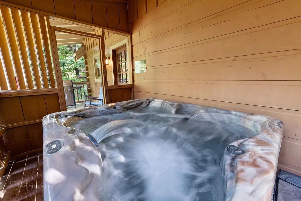 A cozy indoor hot tub nestled against wooden walls, with a doorway leading outside. The scene feels tranquil and intimate, suggesting the perfect spot to relax and share stories after a day of activities.