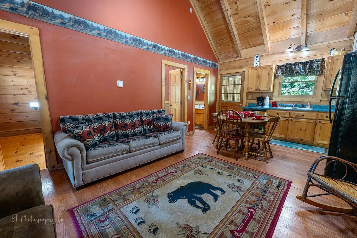 Here, a patterned sofa, a sturdy dining table, a whimsical bear rug, and rich wooden cabinetry create a welcoming and rustic atmosphere. The setting is ideal for family relaxation, dining, and game nights, with visible spaces for both lounging and eating.