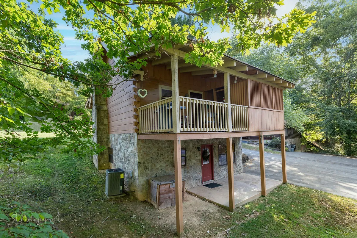 This image features the exterior of Karen’s Cabin, showcasing a wooden balcony with a stone foundation, a distinctive red door, and lush trees surrounding the property. The balcony invites guests to step outside and enjoy the natural mountain setting.