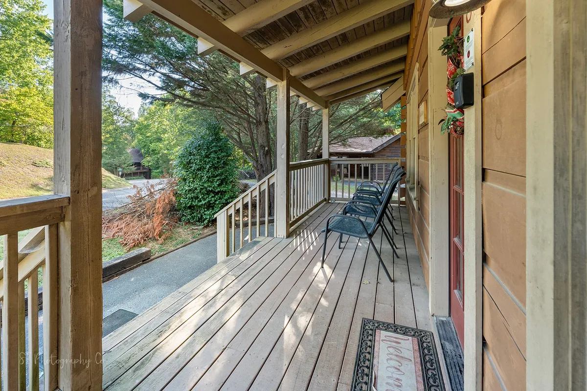 A welcoming front porch with comfortable seating, a cheerful welcome mat, and lush natural surroundings. The porch overlooks a serene outdoor space, perfect for both people and pets to enjoy the fresh mountain air.