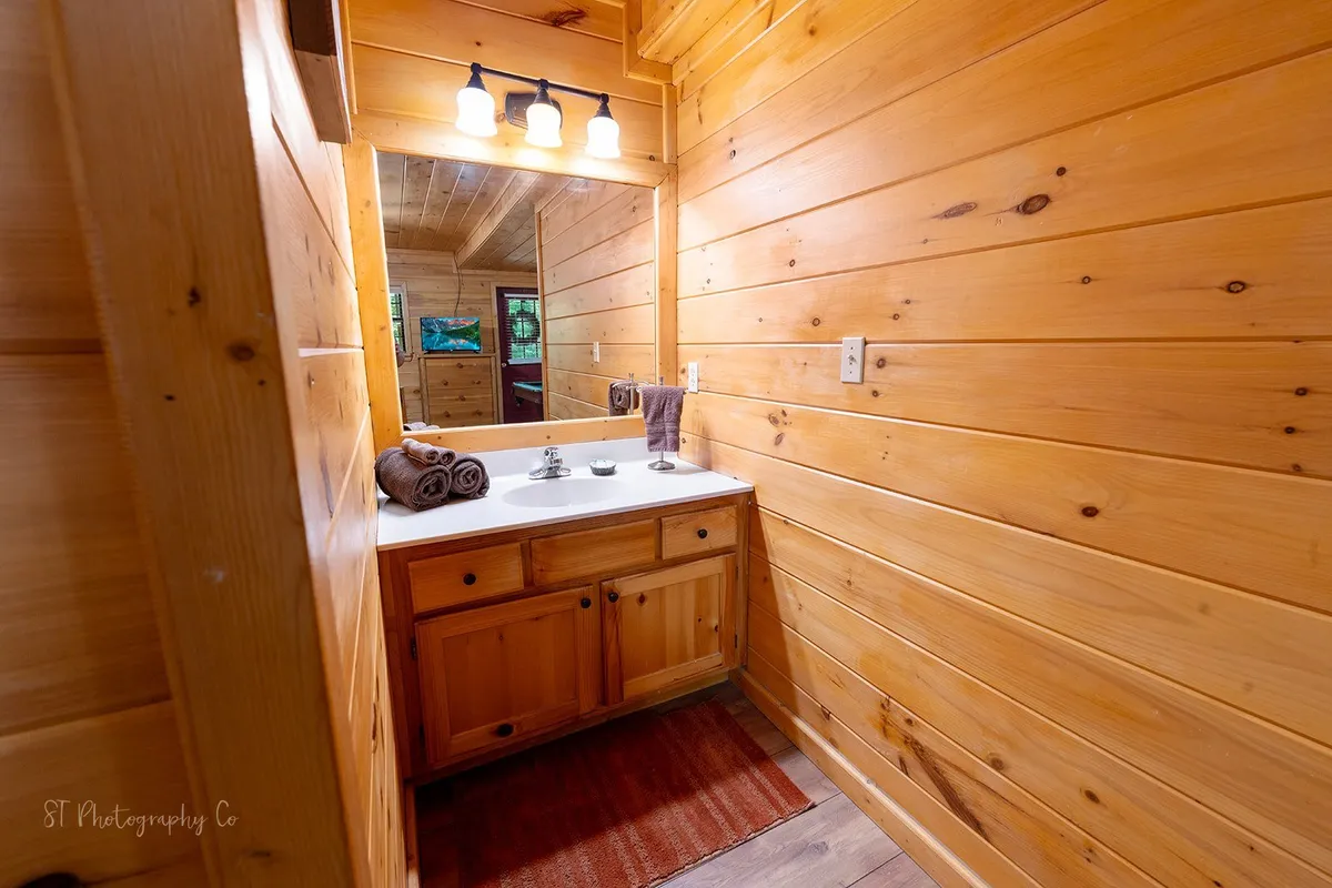 A warmly lit bathroom with a large mirror above a wooden vanity, fluffy towels neatly arranged, and ample space for morning or evening routines. The wooden cabinetry adds a rustic charm while ensuring practicality and comfort.