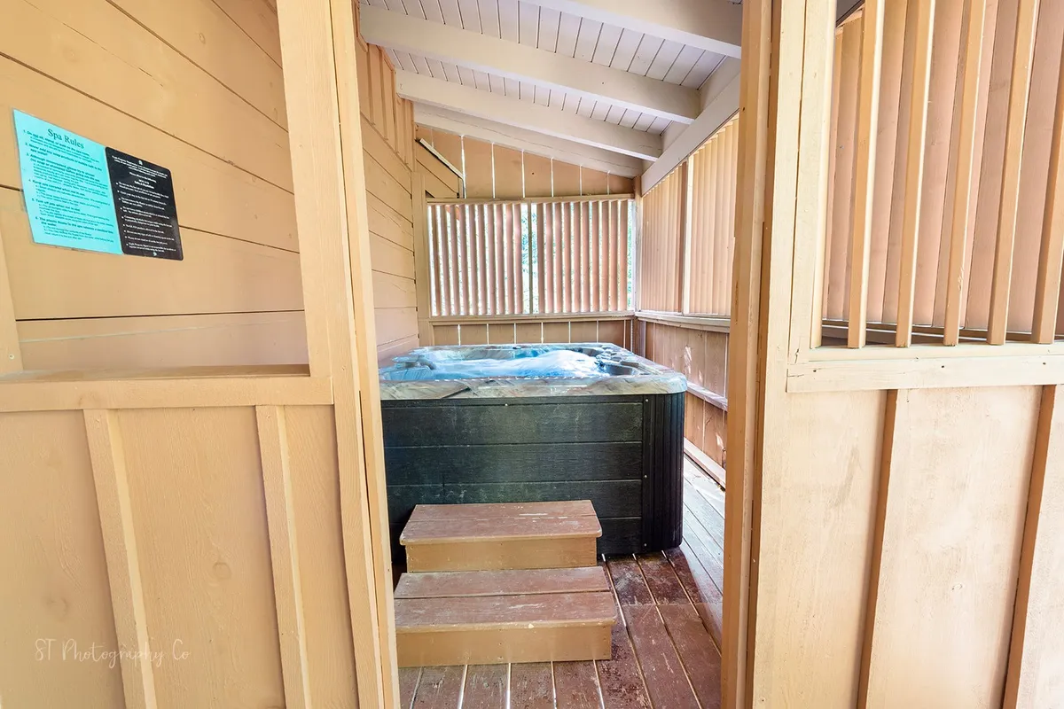 A serene indoor hot tub area with wooden steps, slatted windows offering natural light, and a tranquil ambiance. The hot tub invites guests to relax and rejuvenate after physically demanding activities.