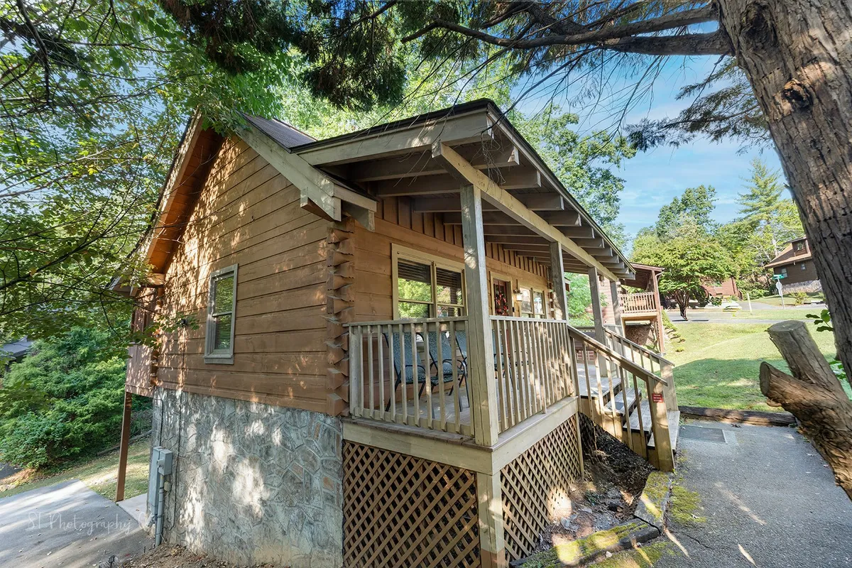 A wooden porch with a sturdy stone foundation and large windows, surrounded by greenery. The ample space provides an outdoor area for lounging, taking in the peaceful mountain landscape, and letting pets enjoy nature safely.