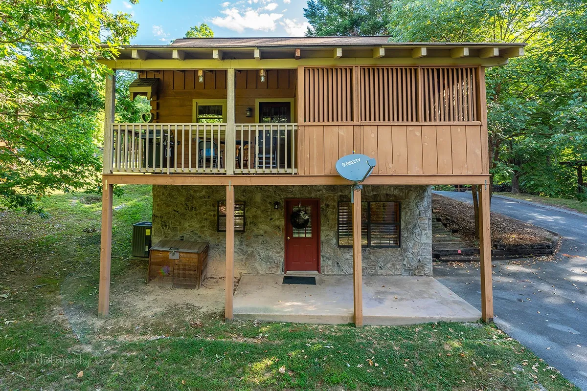 The exterior of the cabin with a welcoming wooden balcony, a striking stone façade, a red door, and lush surrounding greenery. The balcony provides an inviting space for guests to gather and enjoy nature or prepare for a night out.