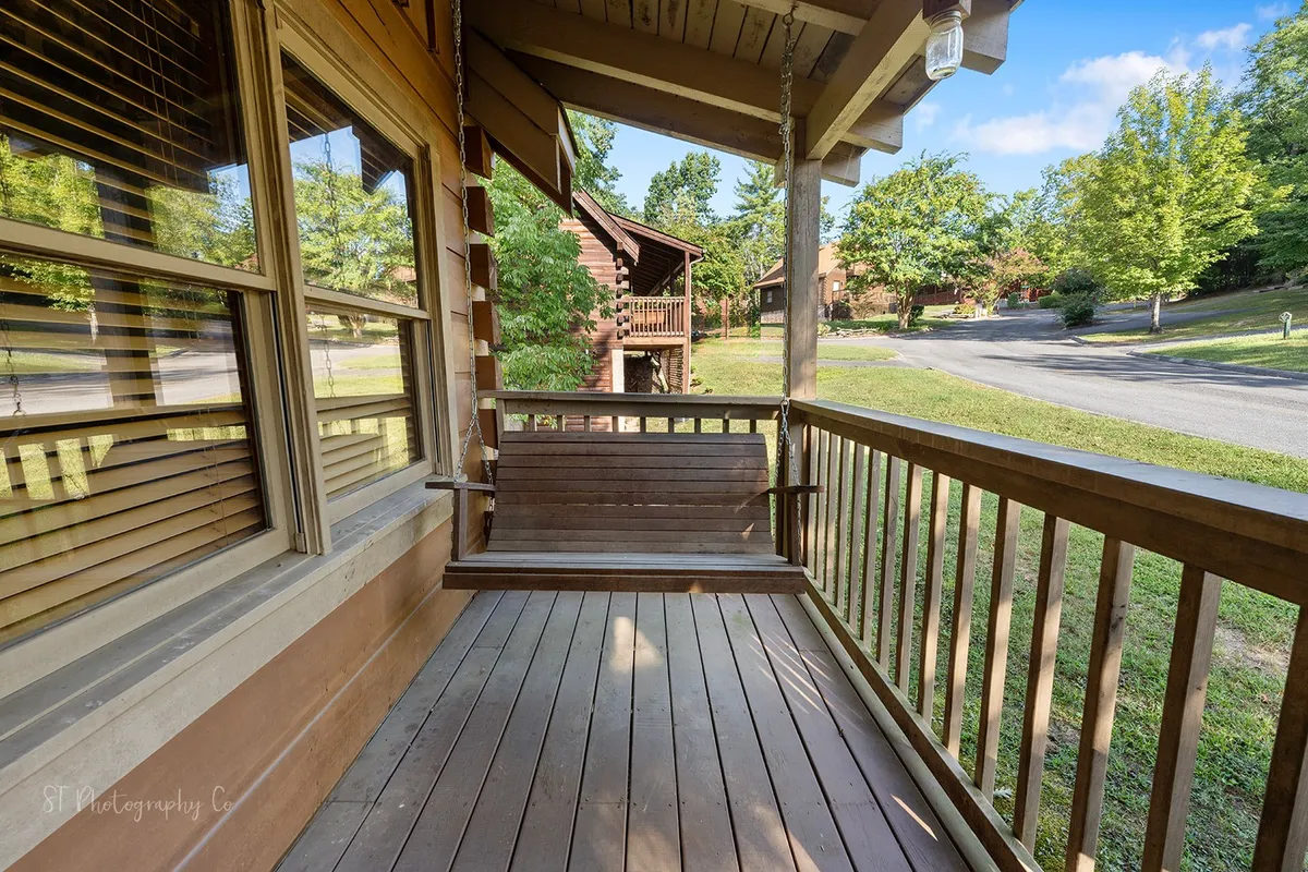 An exterior view highlighting a cozy porch swing on a wooden deck, framed by a rustic railing and surrounded by tall trees. The peaceful setting invites moments of relaxation, reading, or quiet conversation while enjoying nature.
